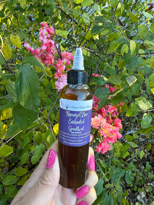 Hand holding a bottle labeled 'Rapunzel hair enchanted growth oil' against a natural background with flowers and leaves.